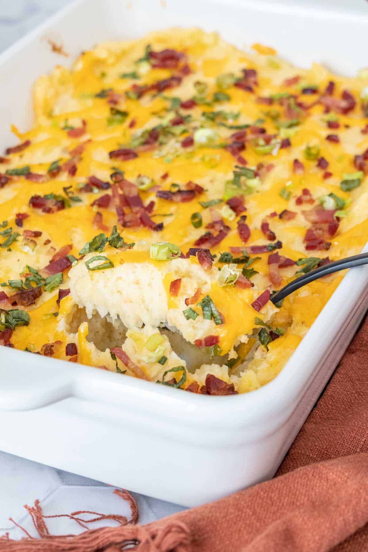 casserole pan of twice baked mashed potatoes with spoon serving