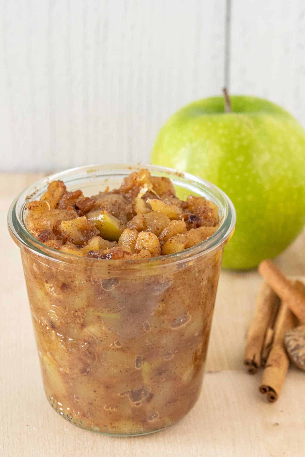 Jar of apple compote with ingredients behind.