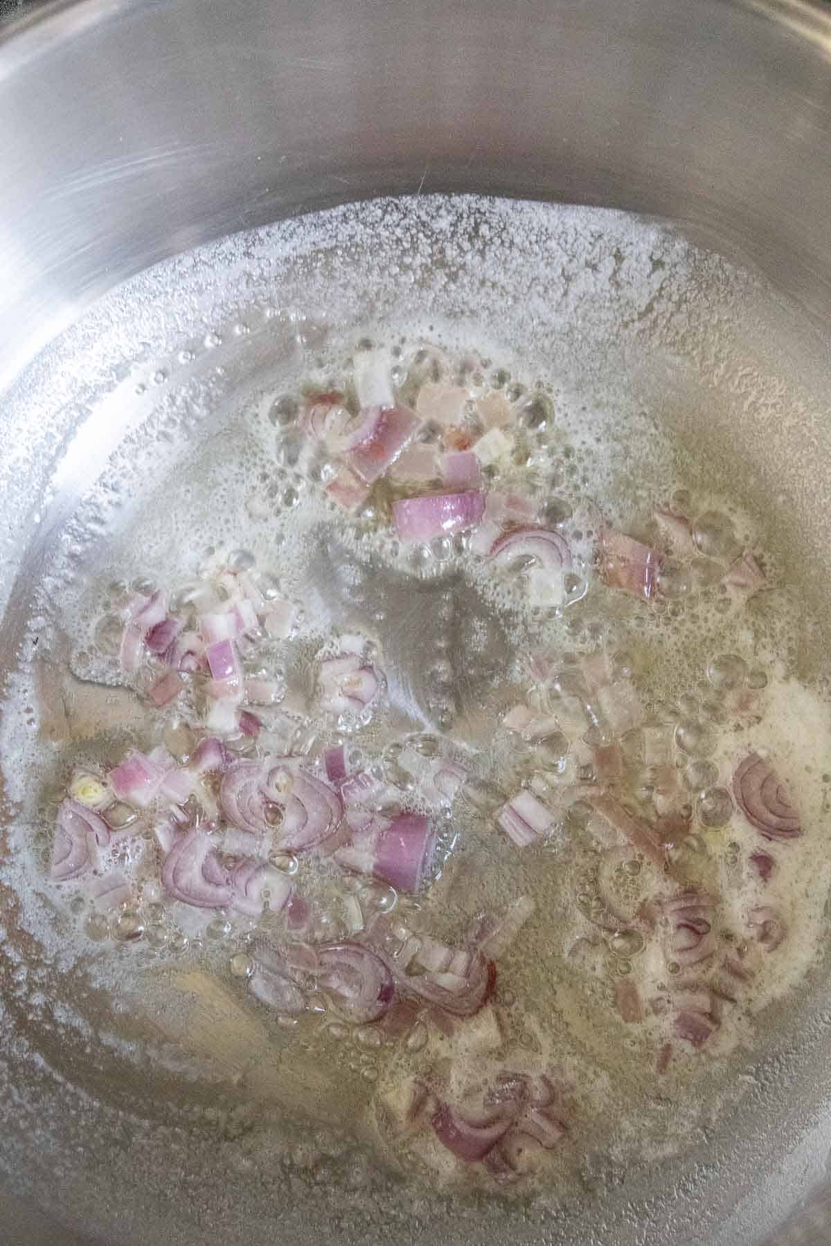 Shallots being sauteed in butter in a stainless steel saute pan.