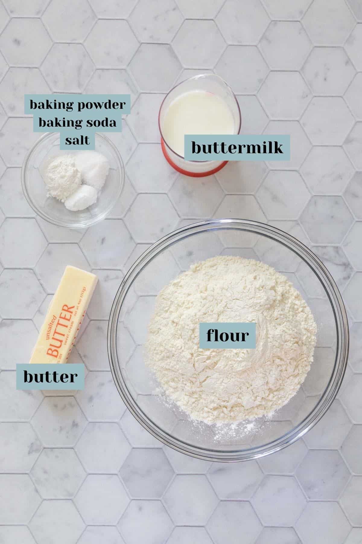 Ingredients for buttermilk biscuits with labels on a tile surface.