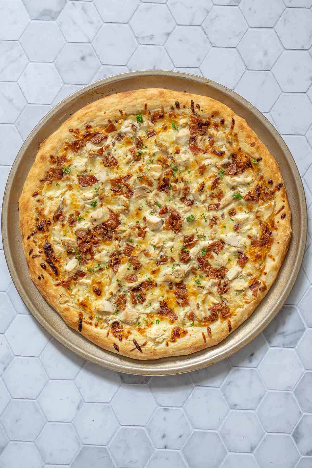 Whole chicken bacon ranch pizza on a tile surface.