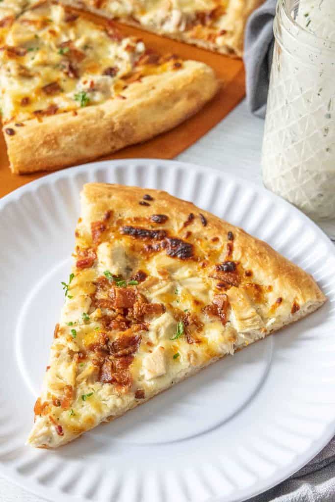 Slice of chicken bacon ranch pizza on a white plate.