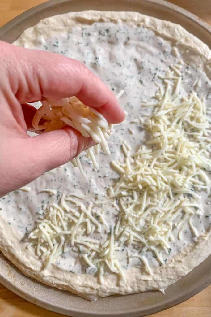 Hand sprinkling cheese onto chicken bacon ranch pizza.