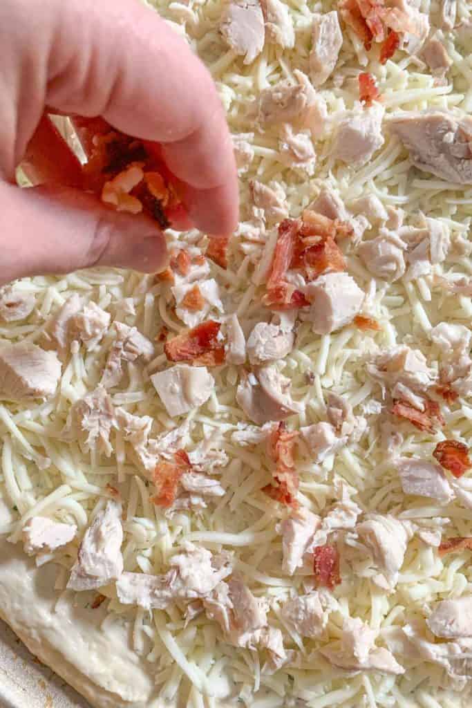 Putting cooked bacon onto pizza before baking.