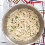 Chicken risotto in a stainless steel cooking pot with a plaid napkin beside.