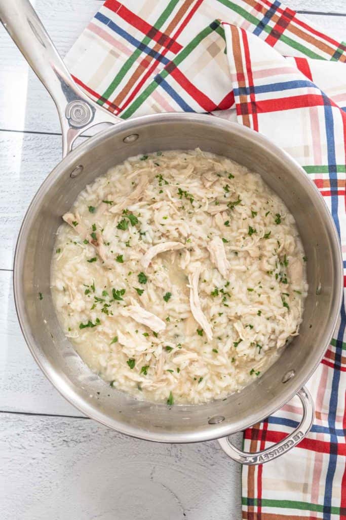 Chicken risotto in a stainless steel cooking pot with a plaid napkin beside.