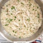 A pan of creamy chicken risotto garnished with chopped herbs, placed on a colorful plaid cloth.