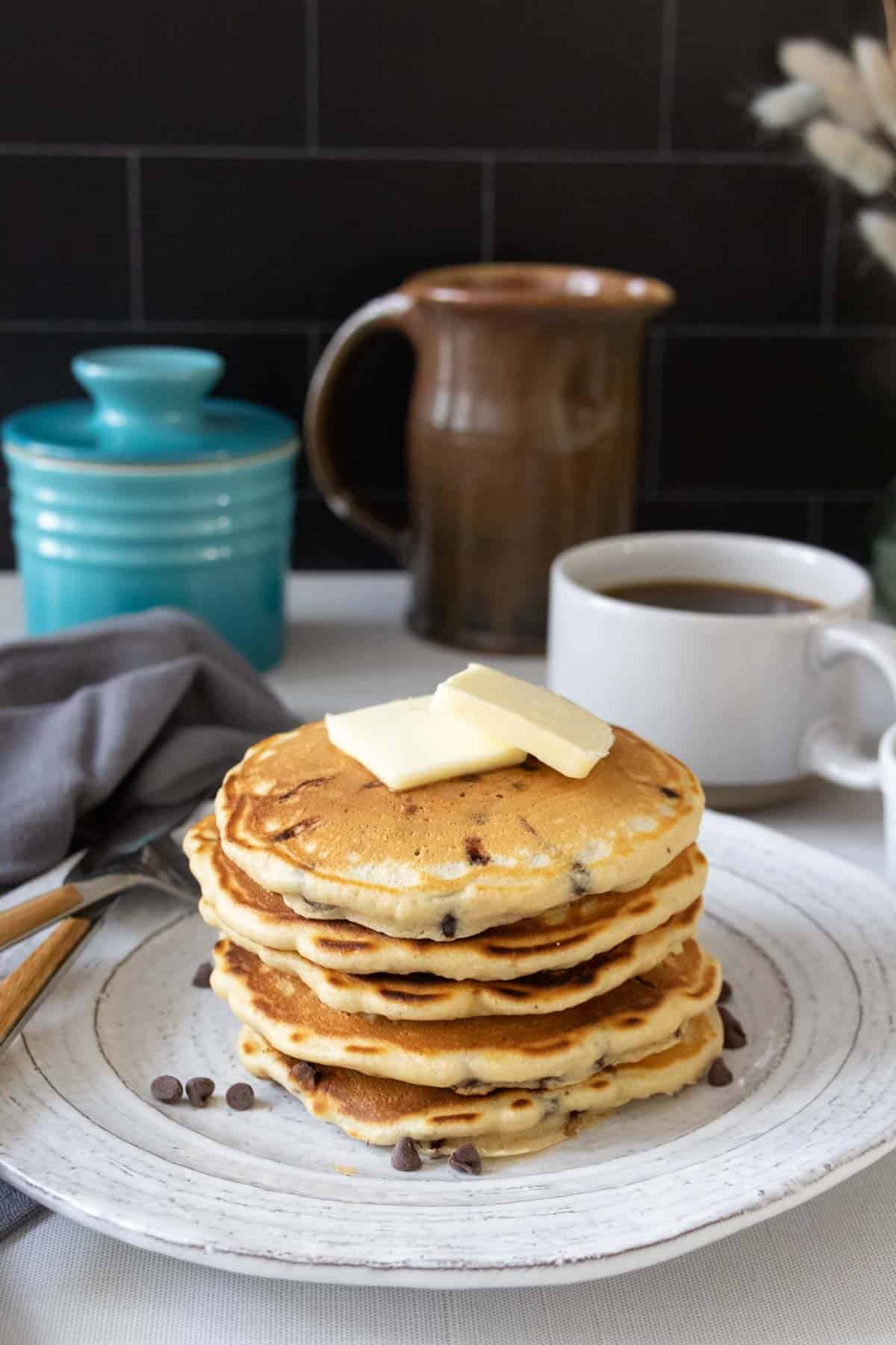 Stack of chocolate chip pancakes on a gray plate with butter on top.