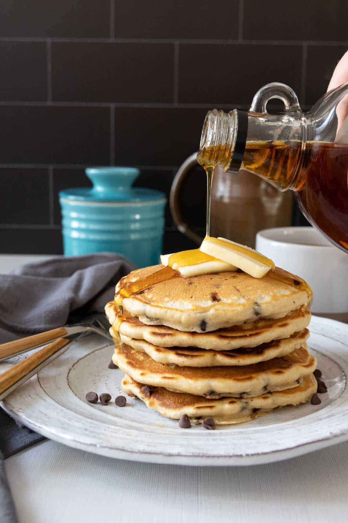 Maple syrup being poured on top of chocolate chip pancakes.