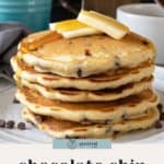 A stack of chocolate chip pancakes topped with butter and syrup, with a blue mug and extra chocolate chips scattered in the background.