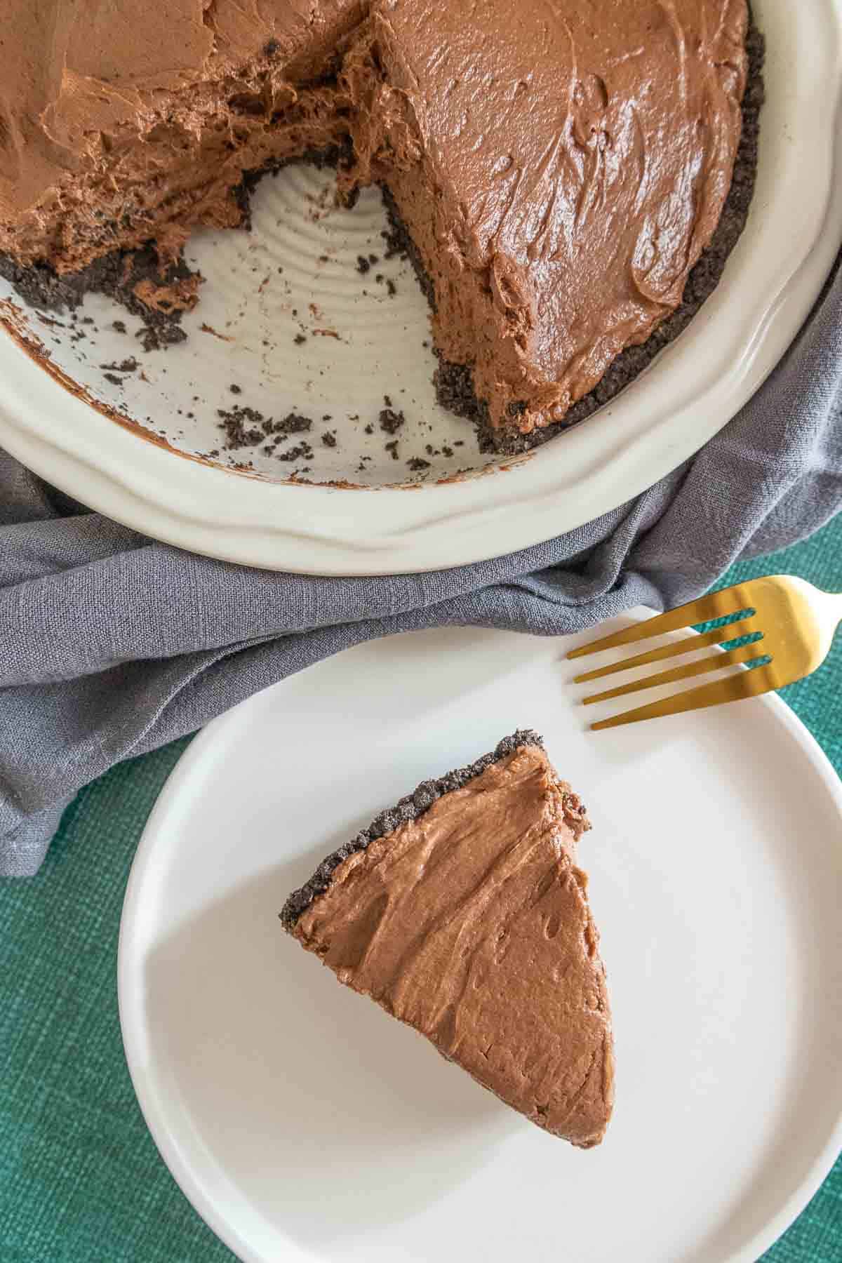 Slice of chocolate peanut butter pie on a plate with rest of pie nearby.