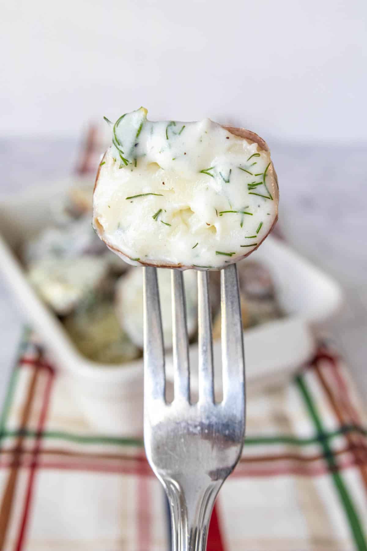 Fork holding up half a small potato with dill cream sauce on it.