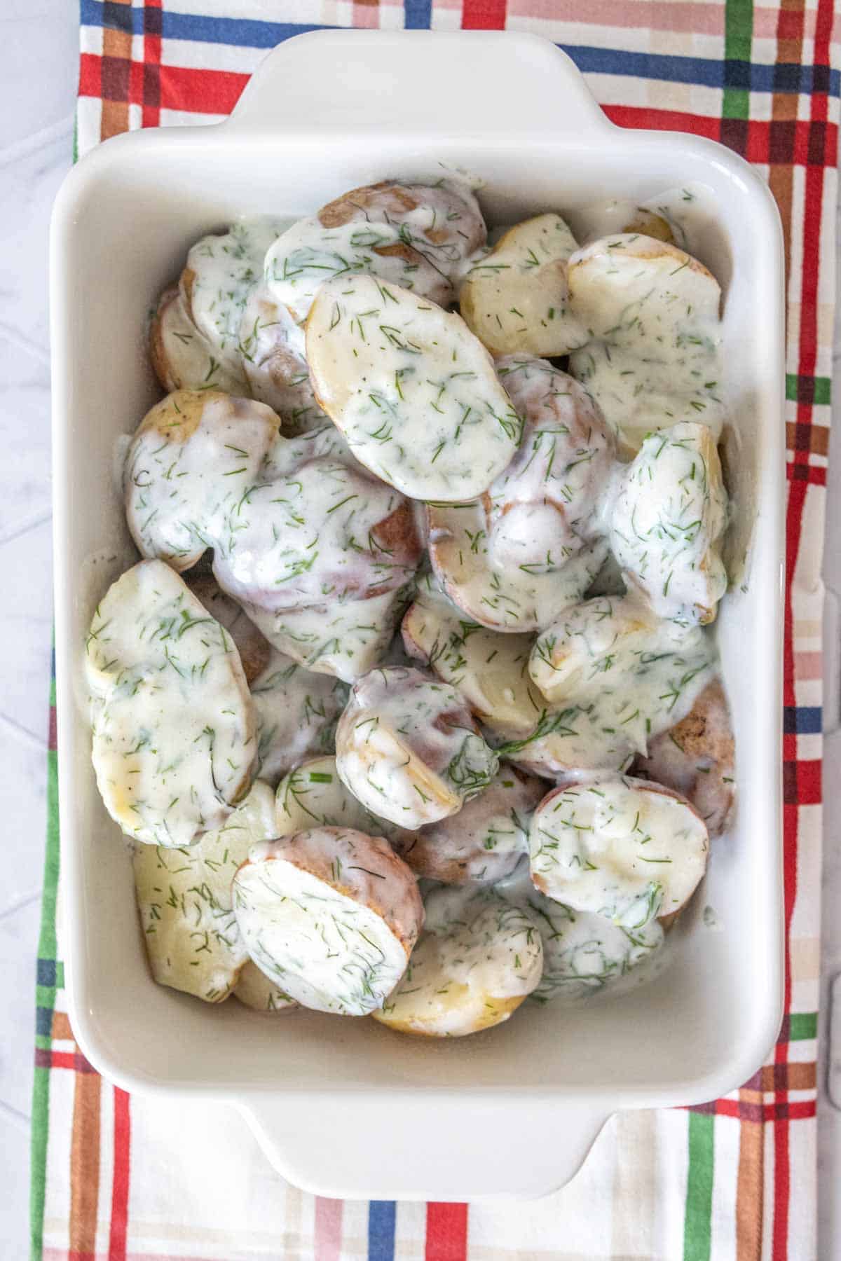 Overhead of dill potatoes in a white dish with a colorful plaid napkin underneath.