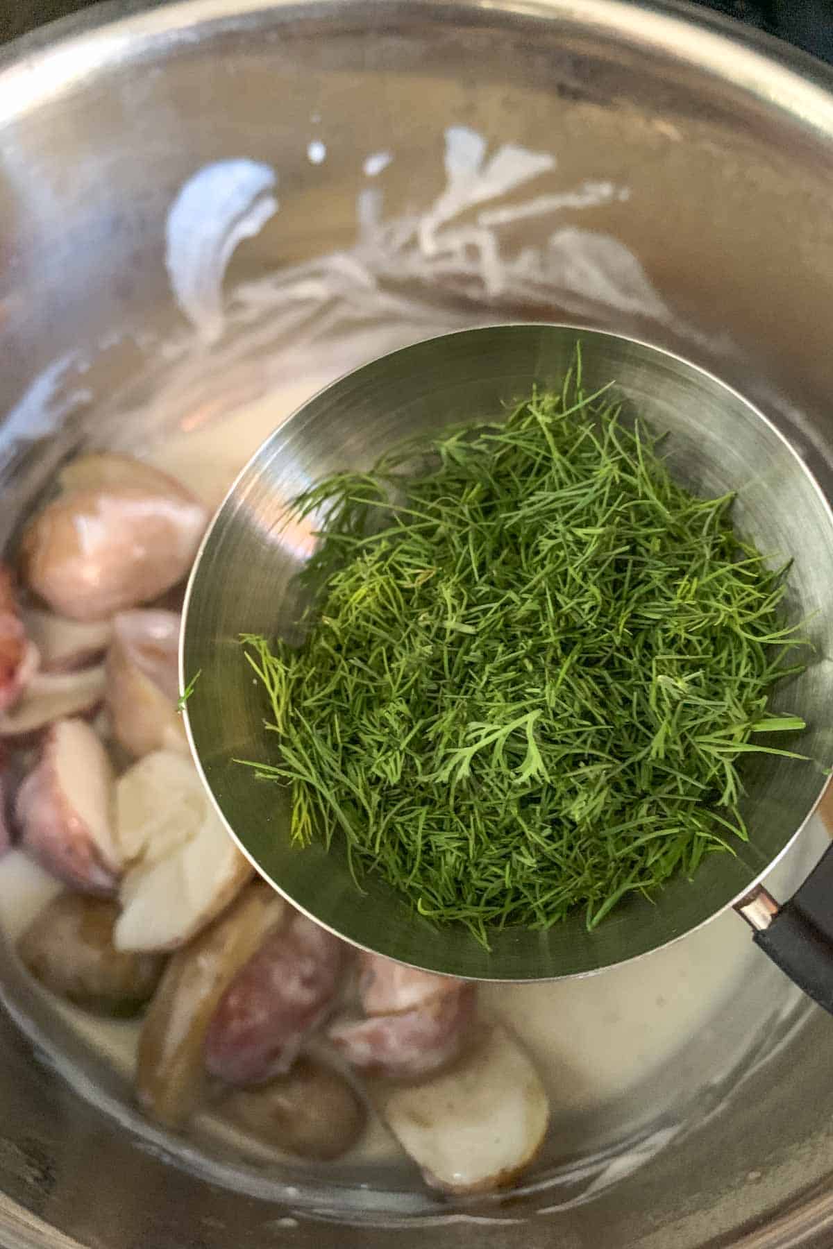 Dill being added to potatoes and cream sauce.