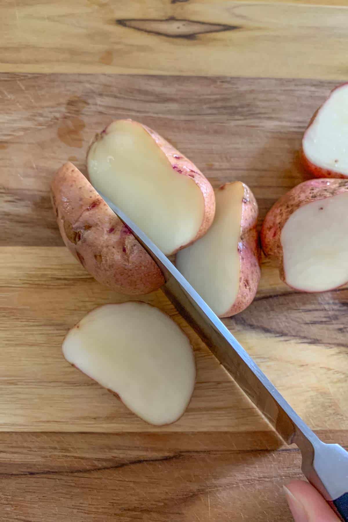 Cutting small potatoes in half on a wooden cutting board.