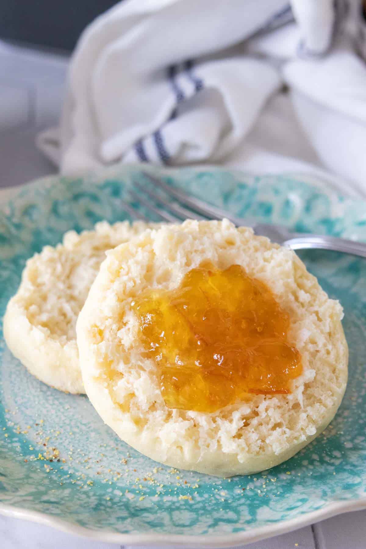 Close up of a split English muffin with marmalade on top.