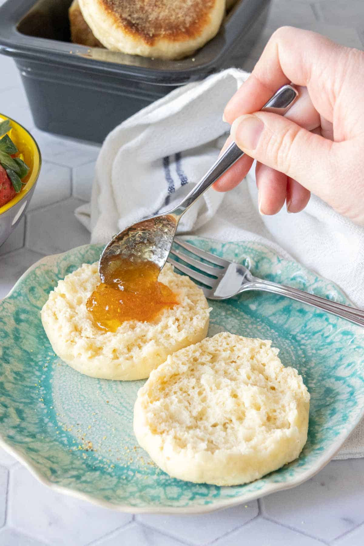 Caucasian hand spooning marmalade onto split English muffin.