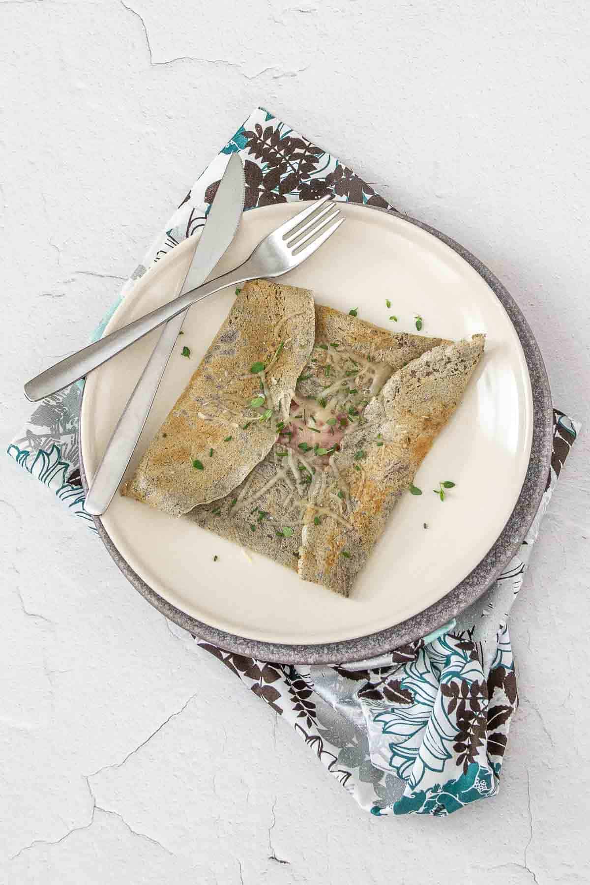 Plate with gluten free crepe on top, filled with ham and cheese.
