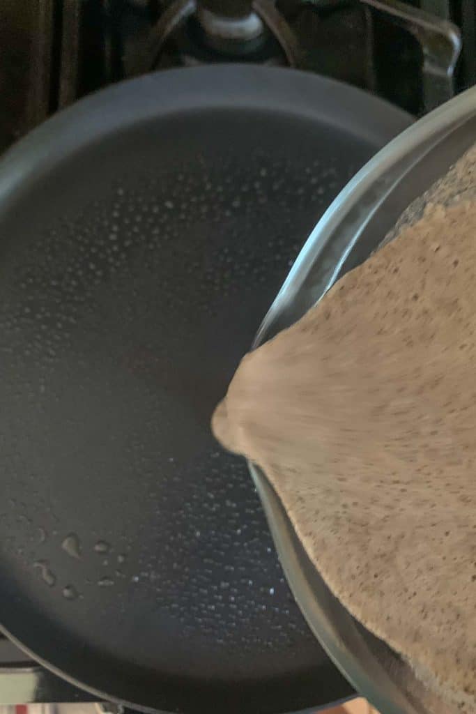 Pouring crepe batter into pan.
