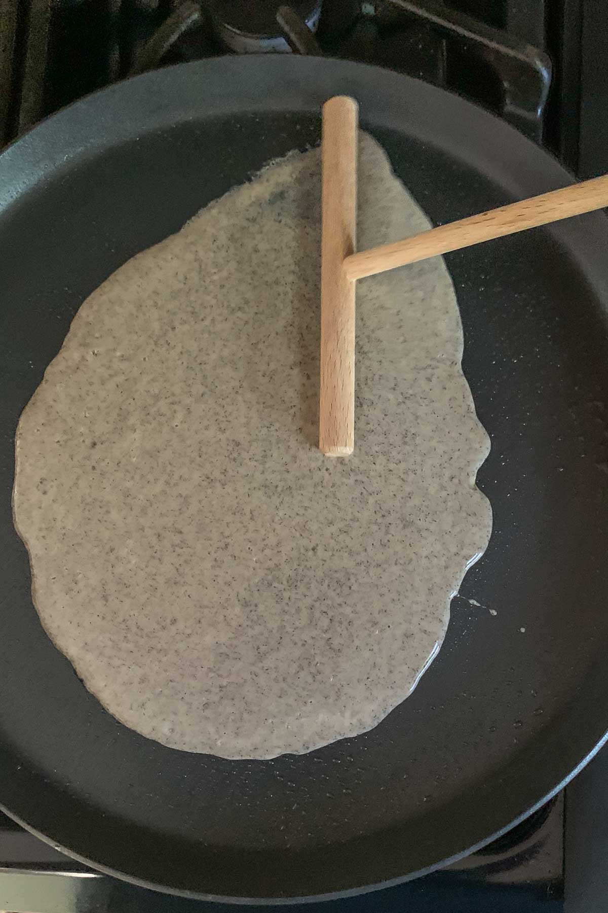 Spreading crepe batter onto a pan using a wooden crepe spreader.