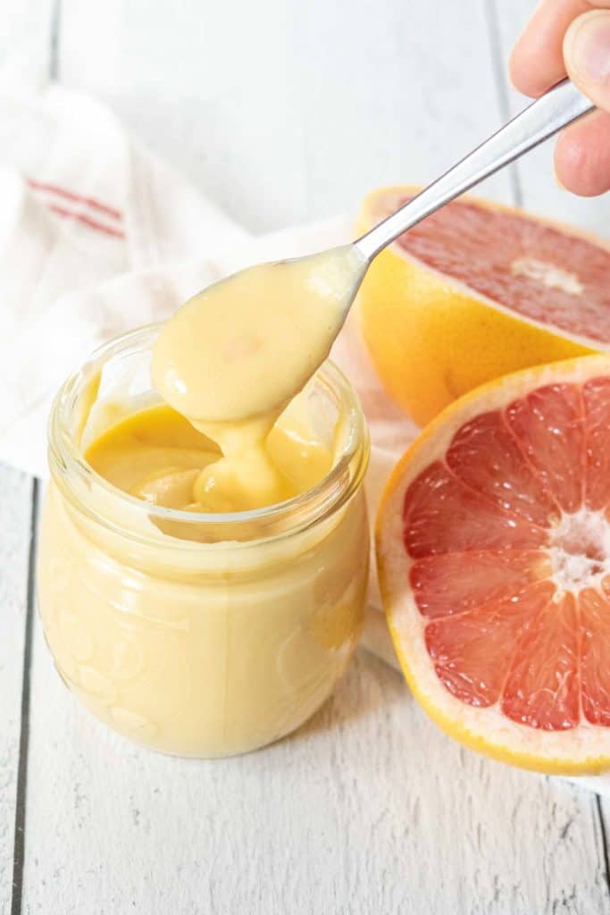 Spoon with a ribbon of grapefruit curd falling back down into the jar.