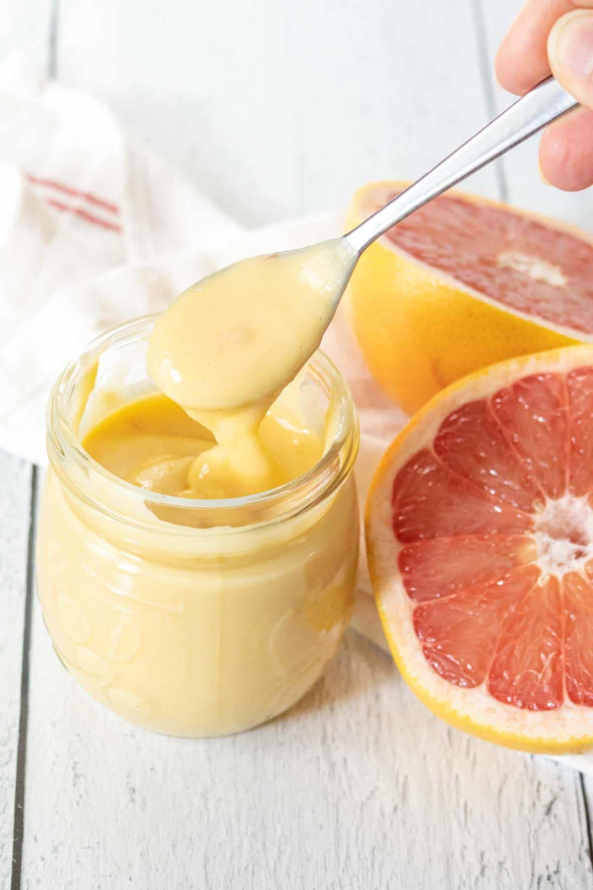 Spoon with a ribbon of grapefruit curd falling back down into the jar.