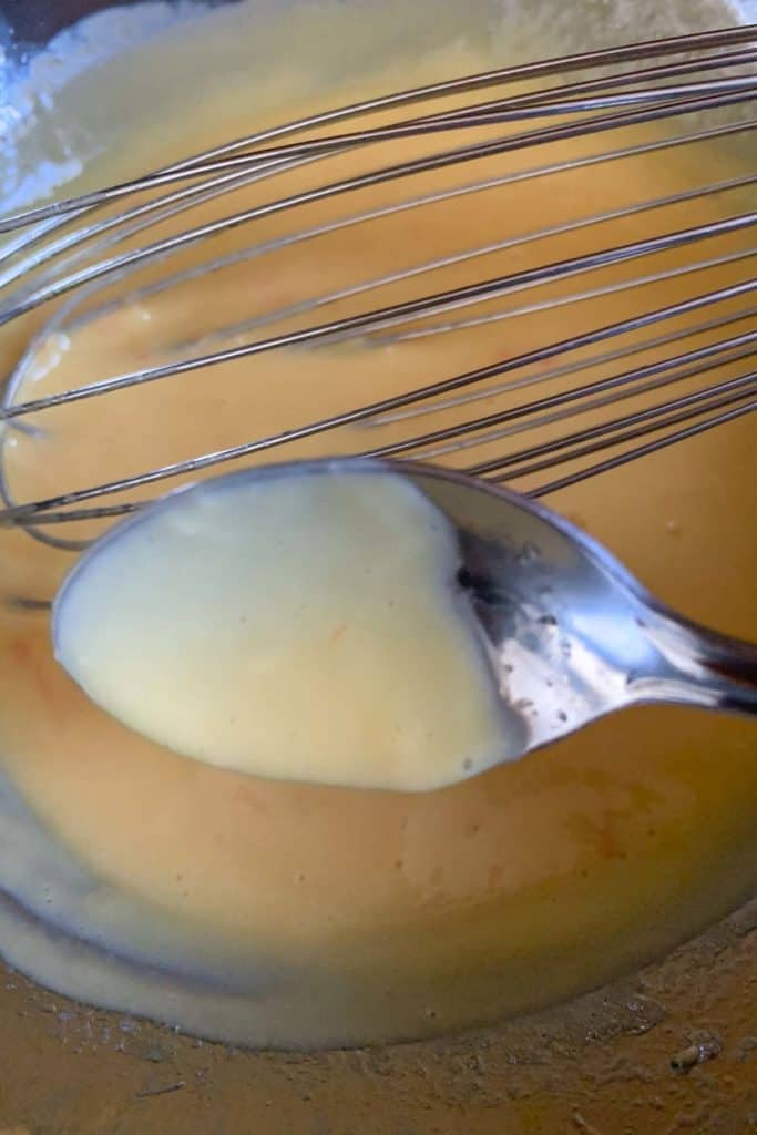 Spoon showing texture of grapefruit curd during cooking.