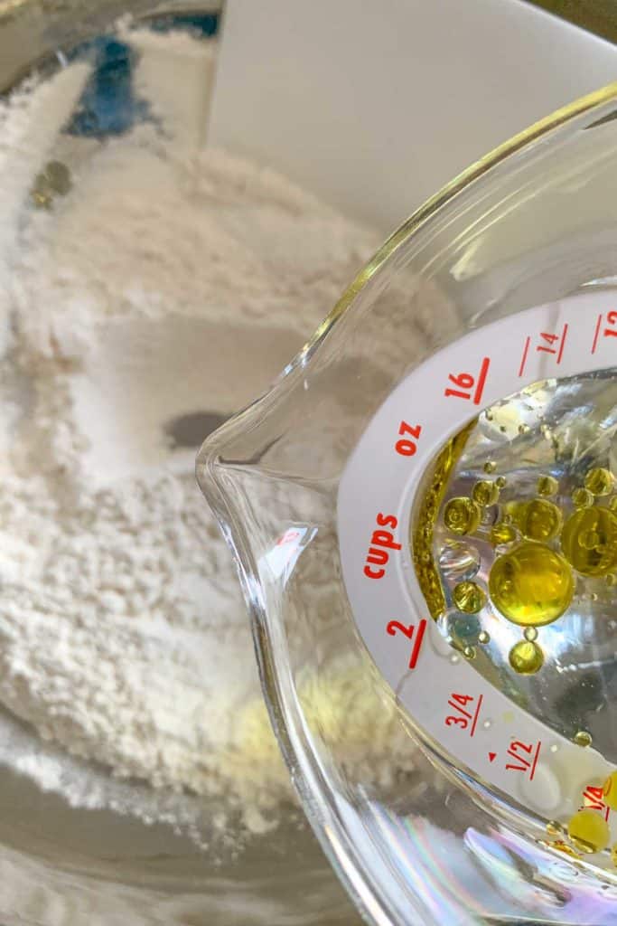 Pouring olive oil and water into pizza dough.