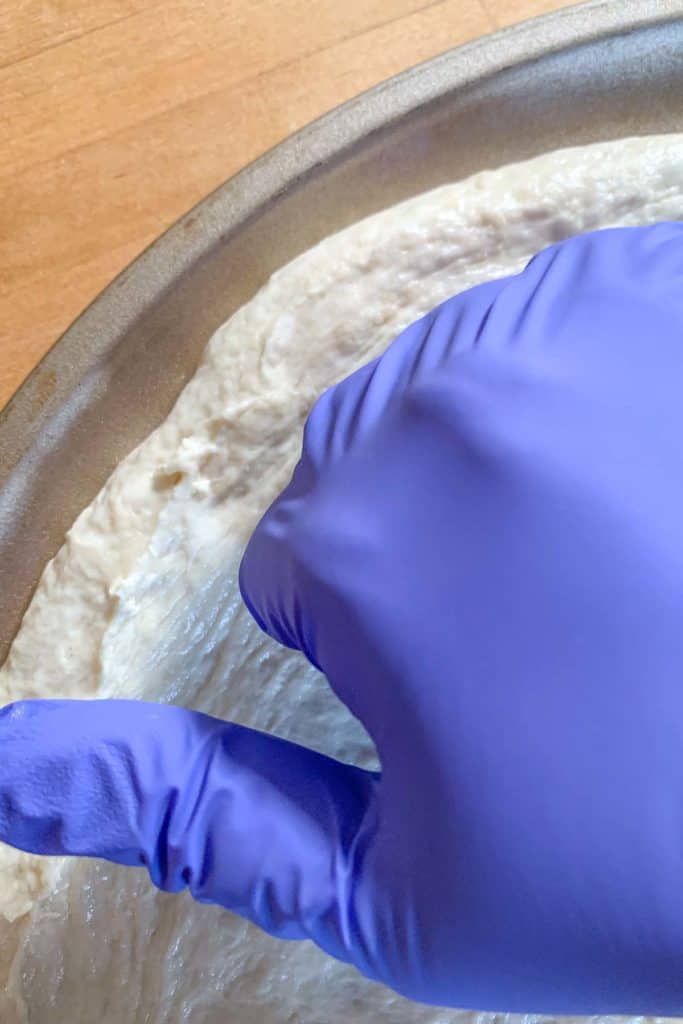Gloved hand pressing out pizza dough edges.