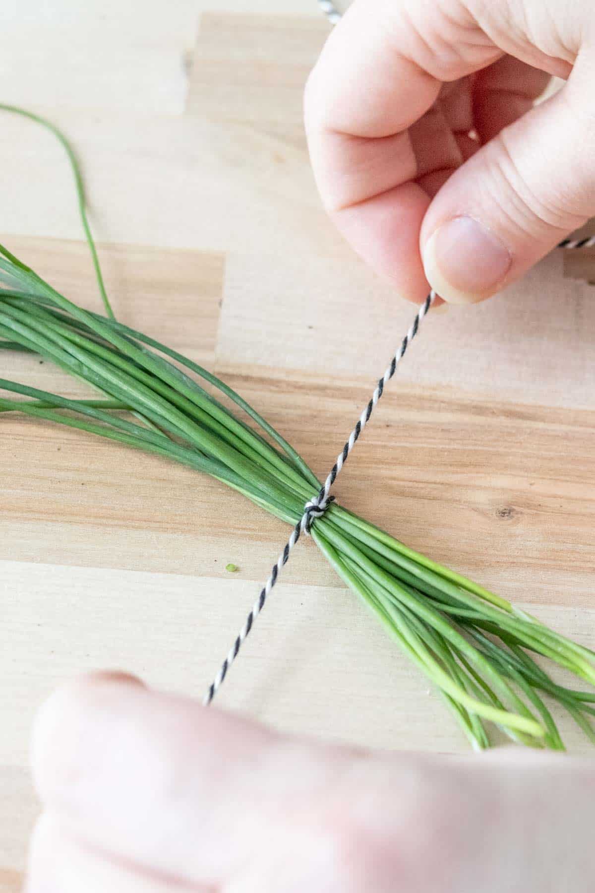 Caucasian hands tying a string around chives.