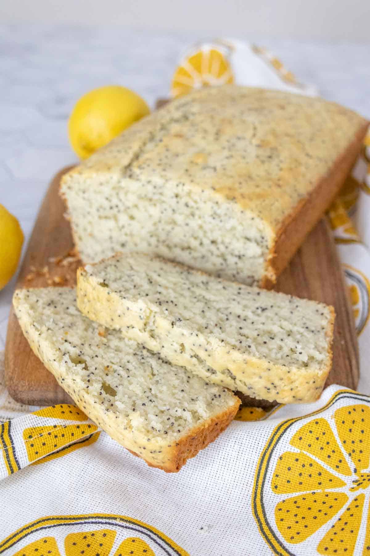 Sliced lemon poppy seed bread on a cutting board with a lemon printed napkin.