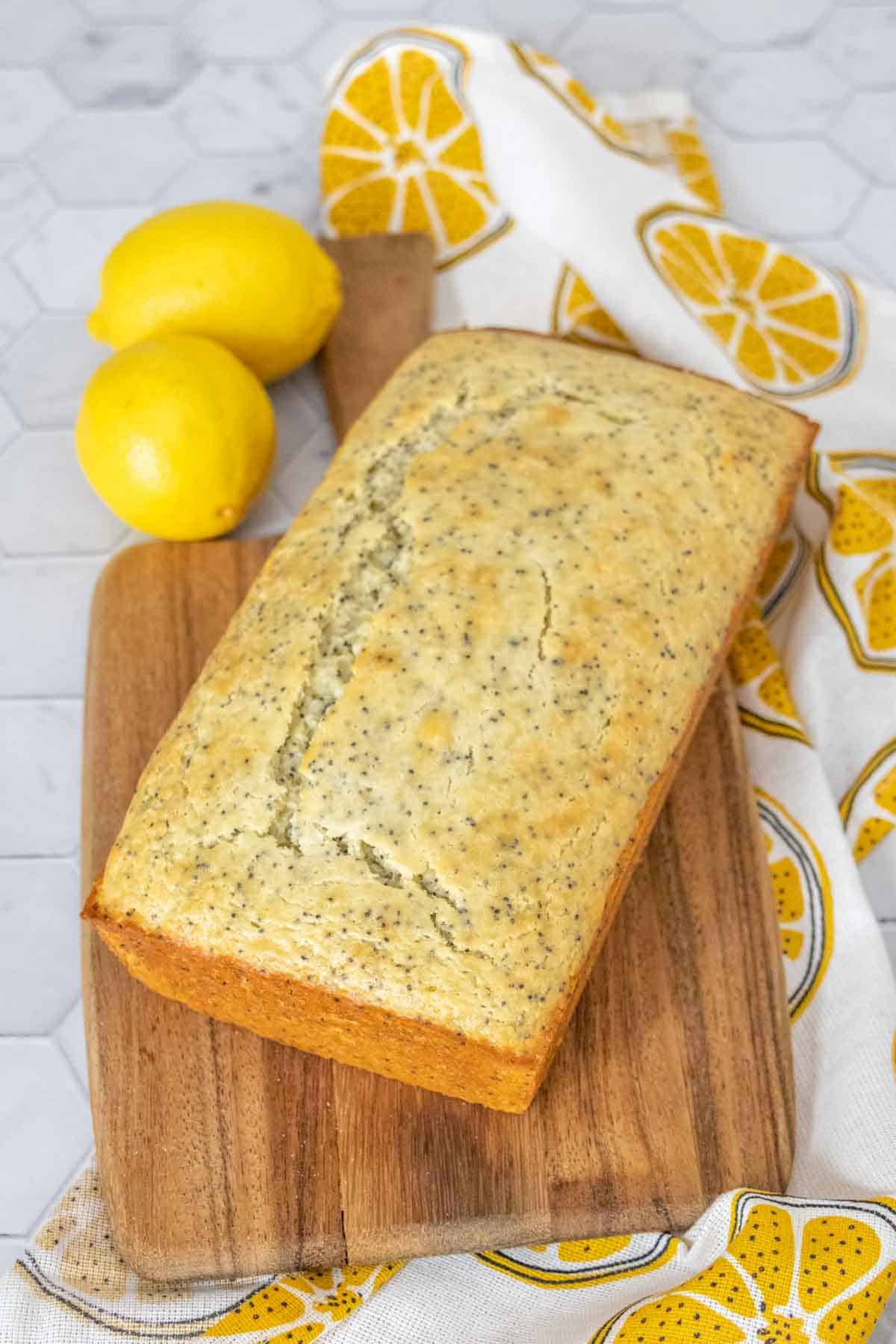 Whole loaf of lemon poppy seed bread on a wooden cutting board.
