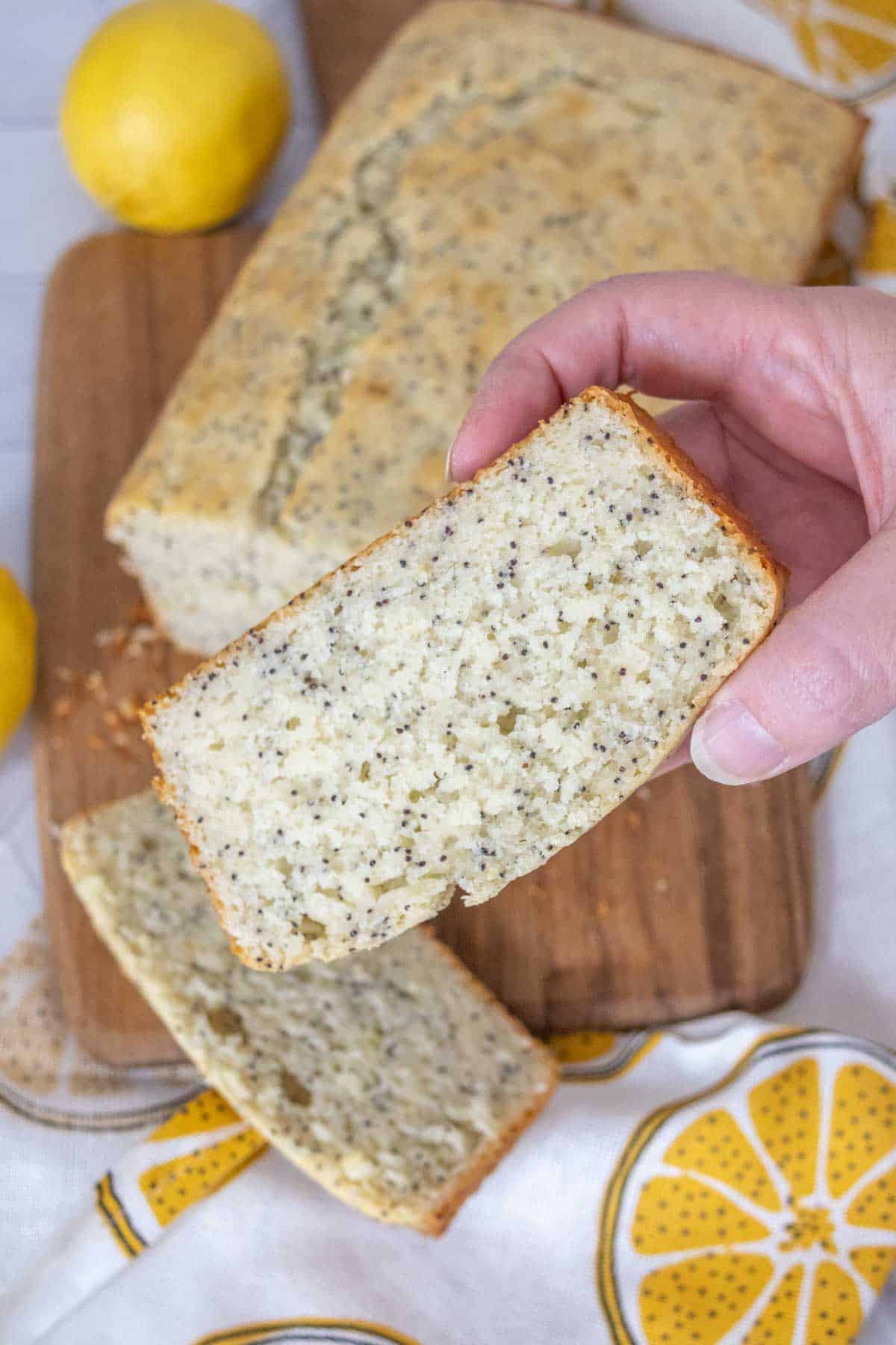 Hand holding up a slice of lemon poppy seed bread.