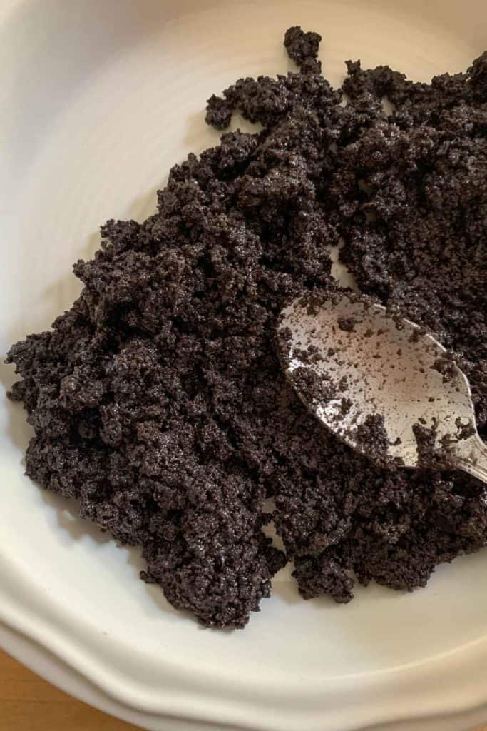 Spoon pressing oreo cookie crust into a pie plate.