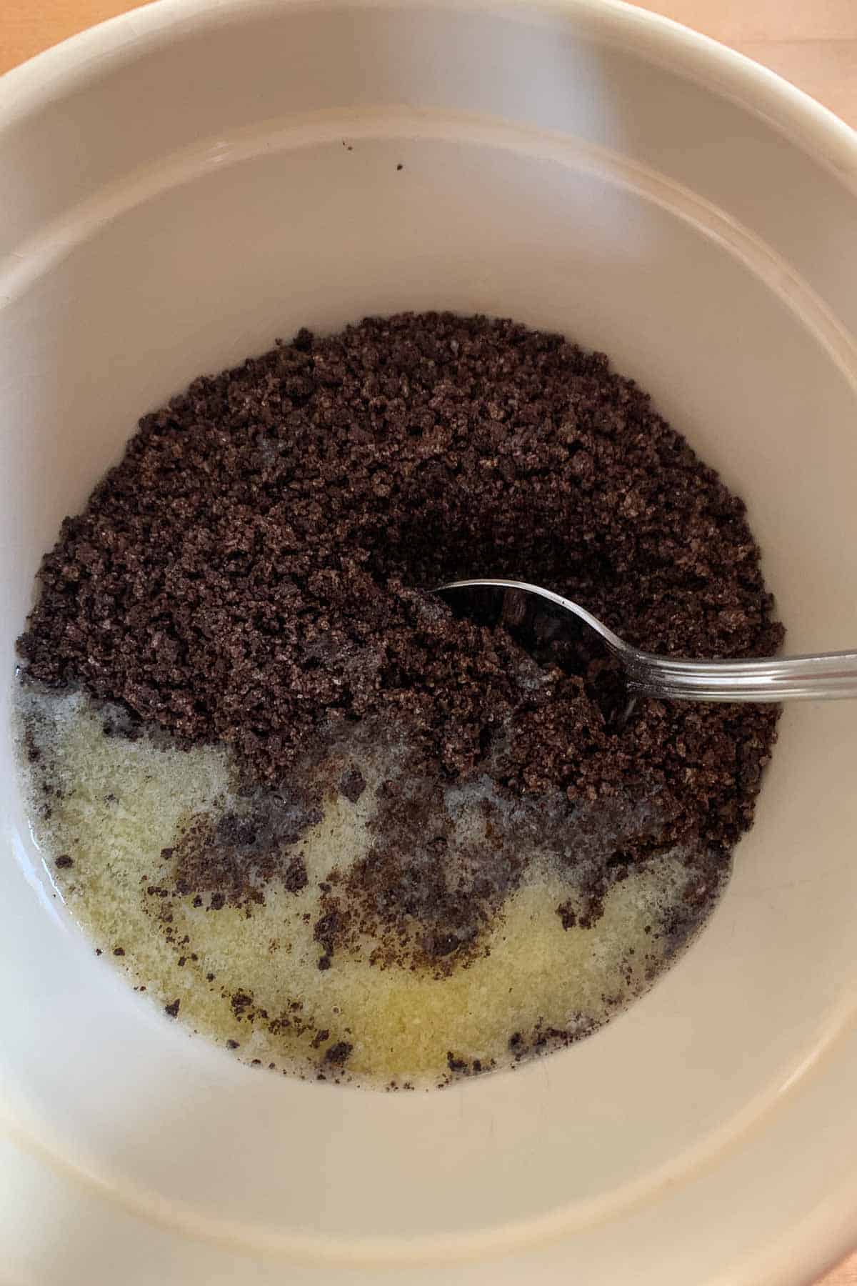Oreo cookie crumbs being mixed with melted butter in a bowl.