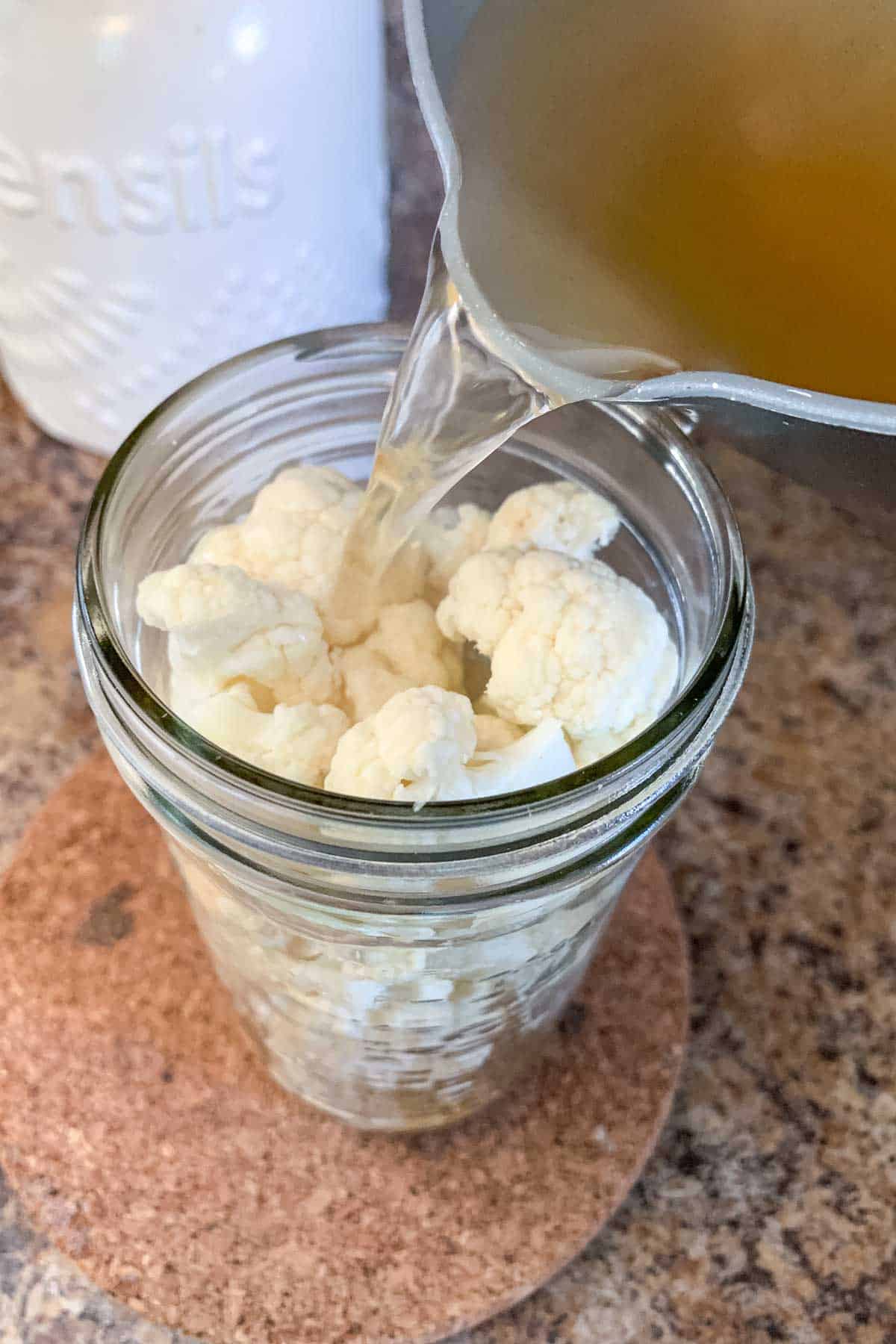 Pouring hot brine into a jar of cauliflower for pickles.