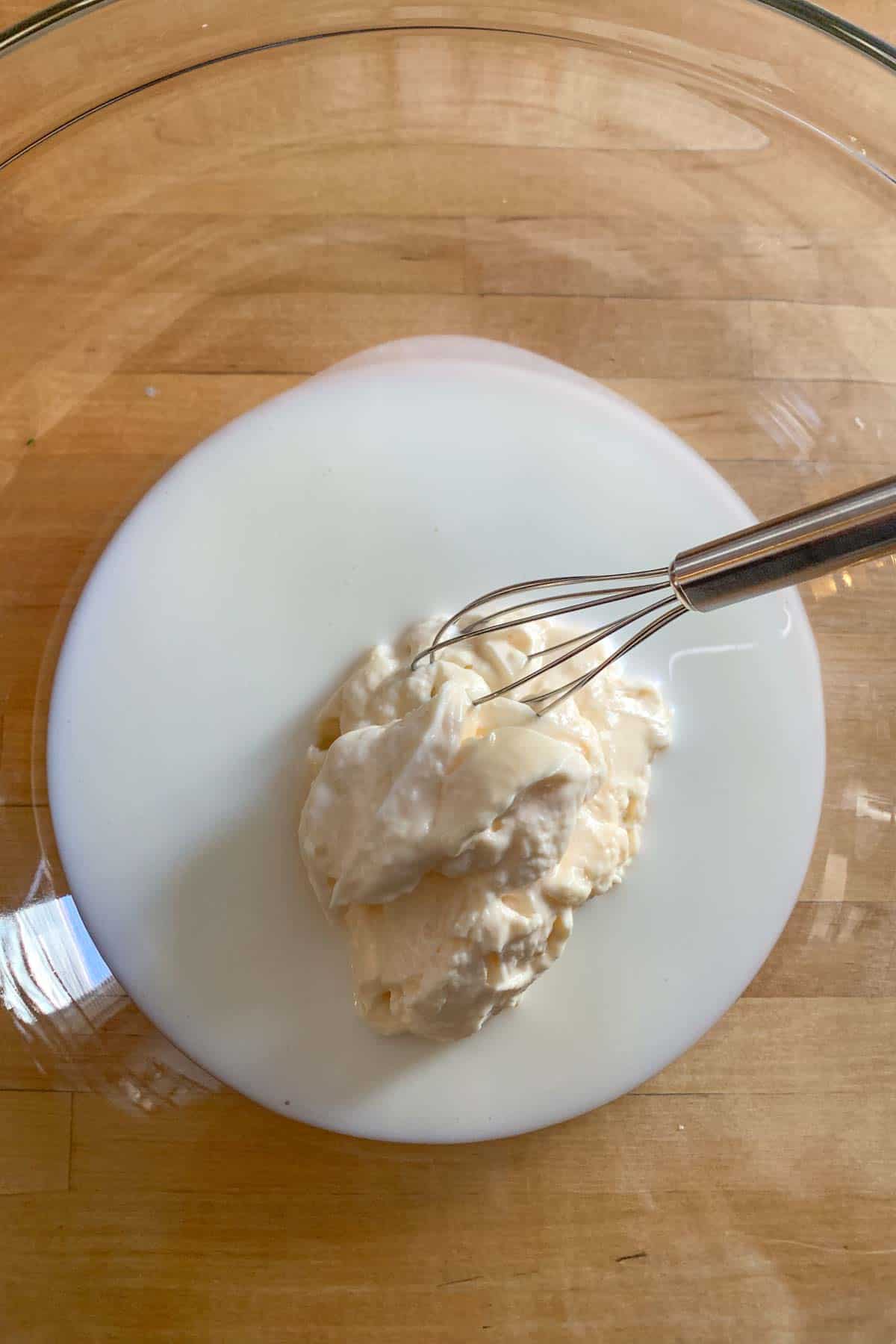 Buttermilk and mayonnaise in a glass bowl on a wooden countertop.