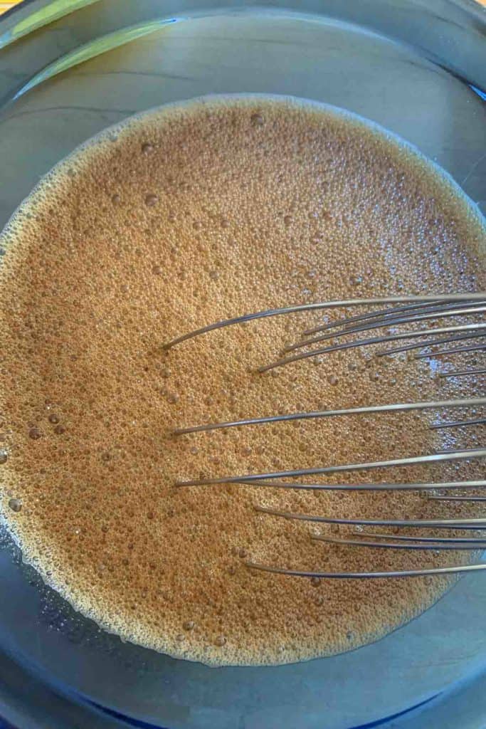Blue bowl with molasses, hot water, and baking soda whisked together to make foamy.