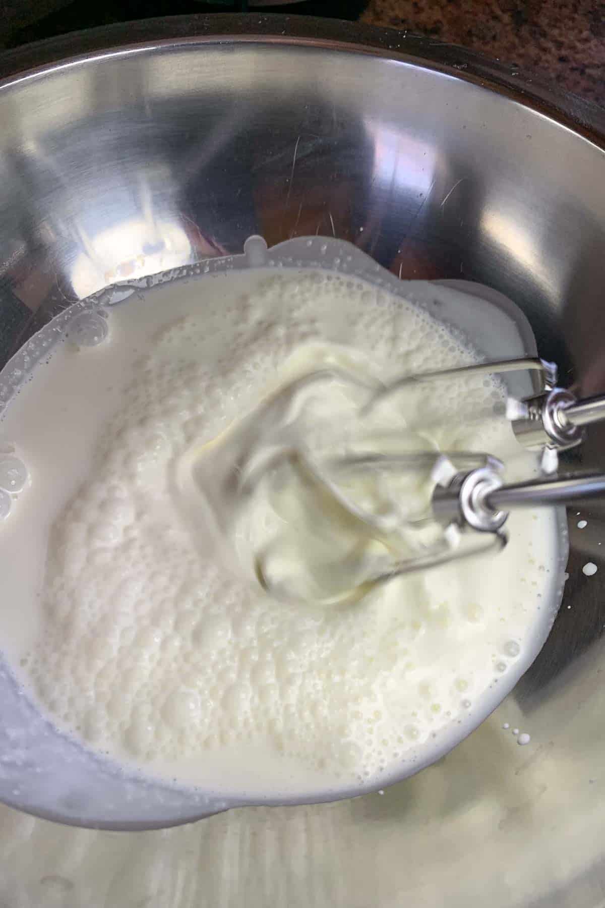 Cream being whipped in a metal bowl using a hand mixer.