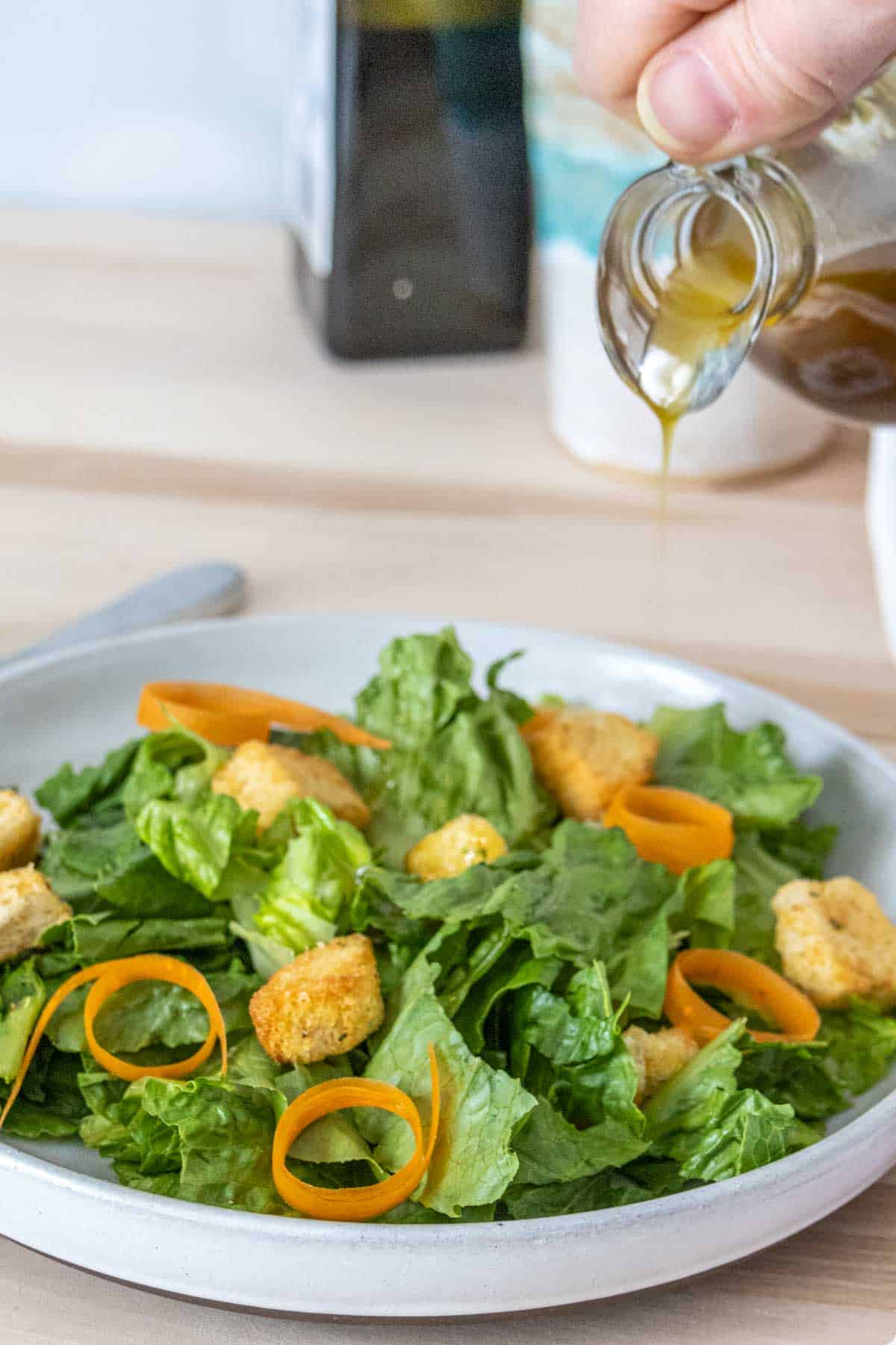 Pouring balsamic vinaigrette onto a green salad.