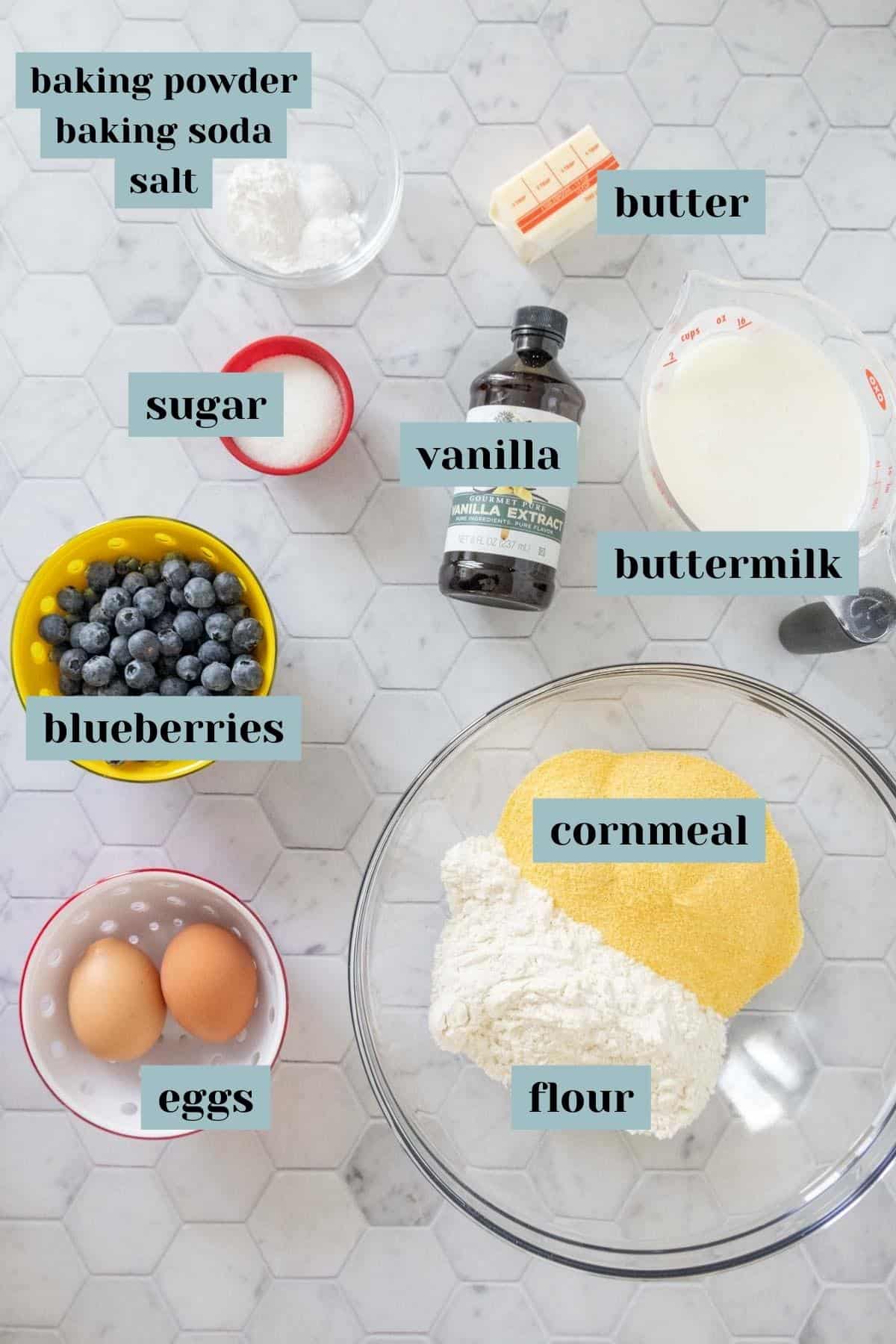 Ingredients for blueberry pancakes on a tile surface with labels.