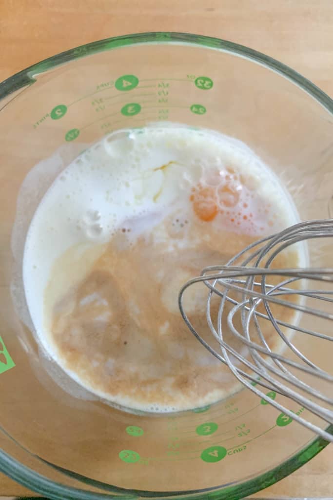 Glass measuring cup with wet ingredients for blueberry pancakes.
