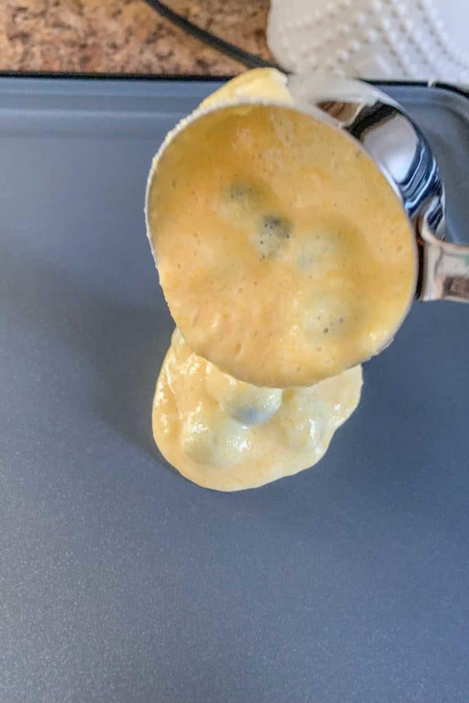 Pouring blueberry pancake batter onto a griddle.