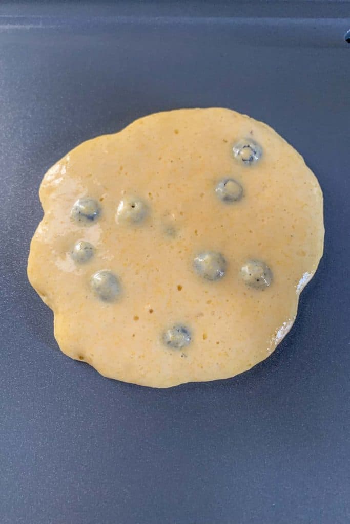 Blueberry pancake cooking on a griddle.