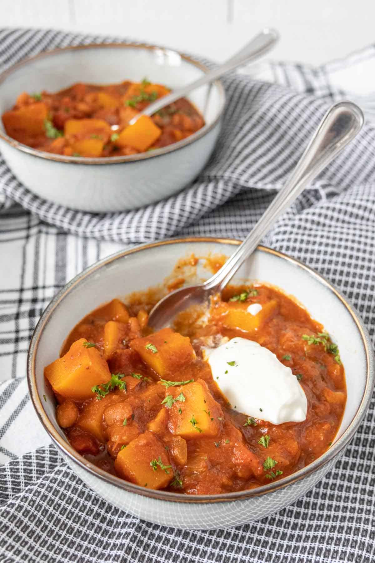 Two bowls of butternut squash chili, front bowl with sour cream.