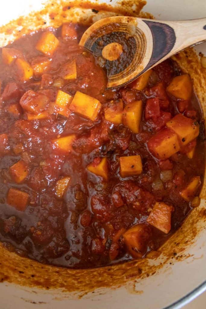 Stirring butternut squash chili in dutch oven.