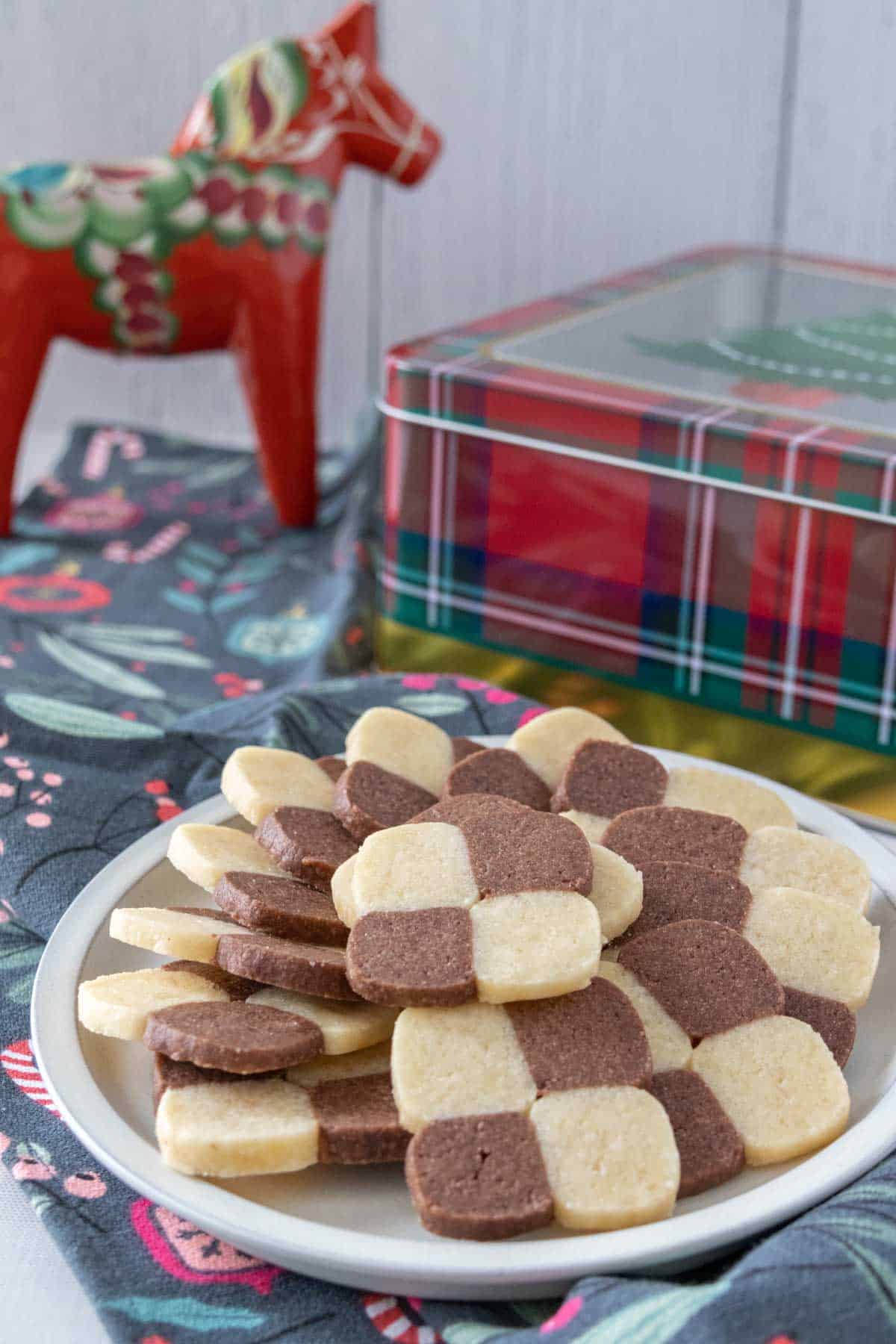 Plate of checkerboard cookies with a cookie tin and dala horse behind.