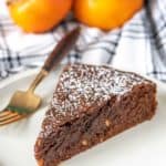 Slice of chocolate persimmon cake on a plate with a fork and persimmons behind.