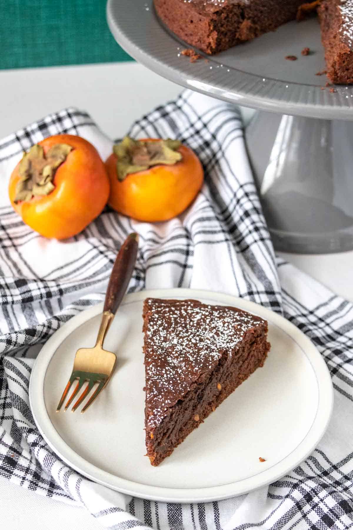 Slice of chocolate persimmon cake on a gray plate with a black plaid napkin.