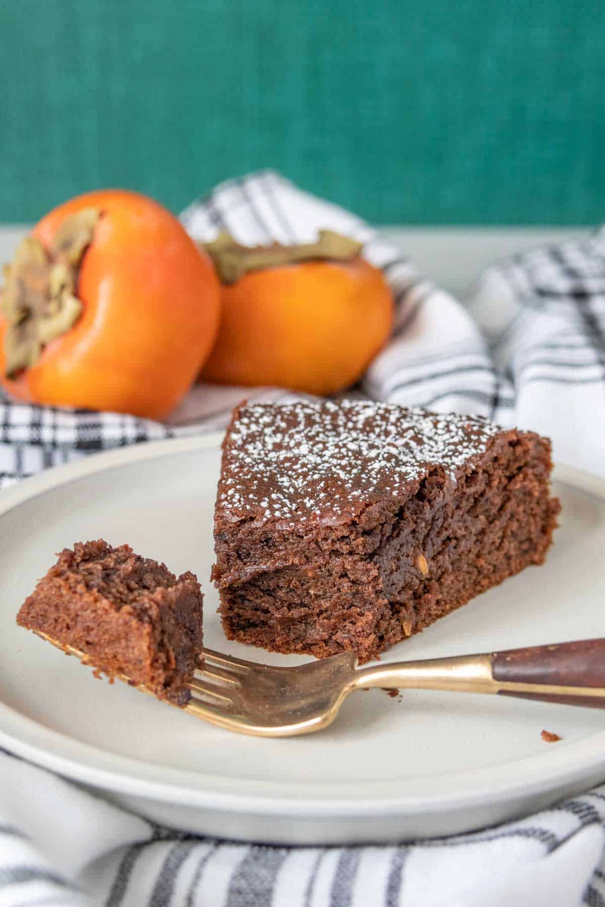 Slice of chocolate persimmon cake with bites taken and a piece on a fork.